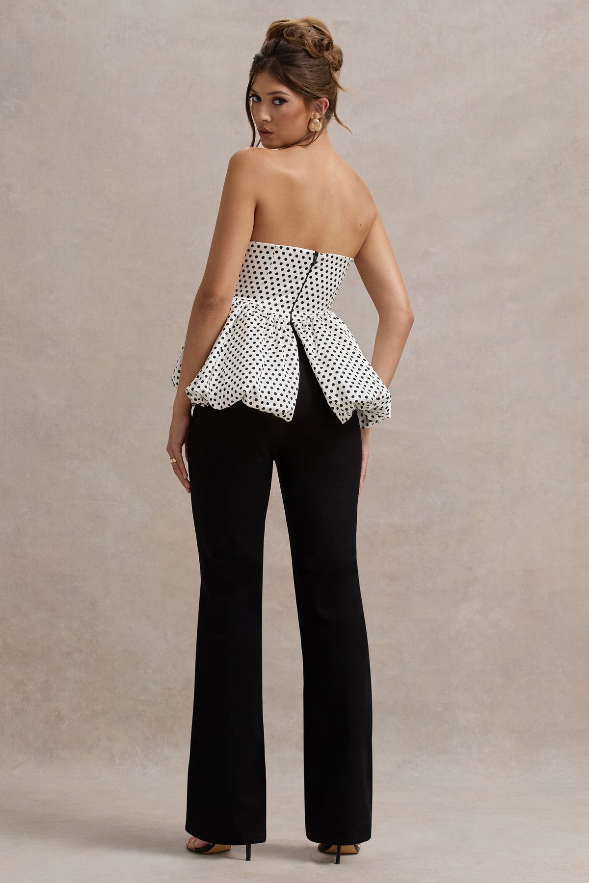 Divina | Weißer und schwarzer Jumpsuit mit Polka-Dots, trägerlos und mit Rüschen.